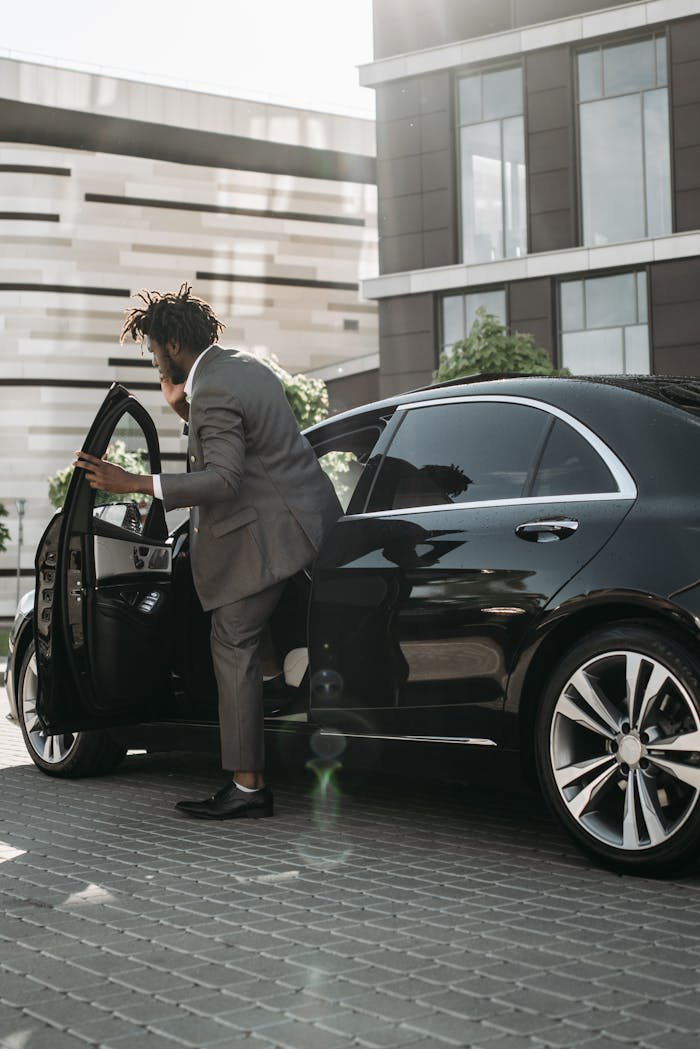 Stylish adult man in gray suit stepping out of a luxury black car in a modern city environment.